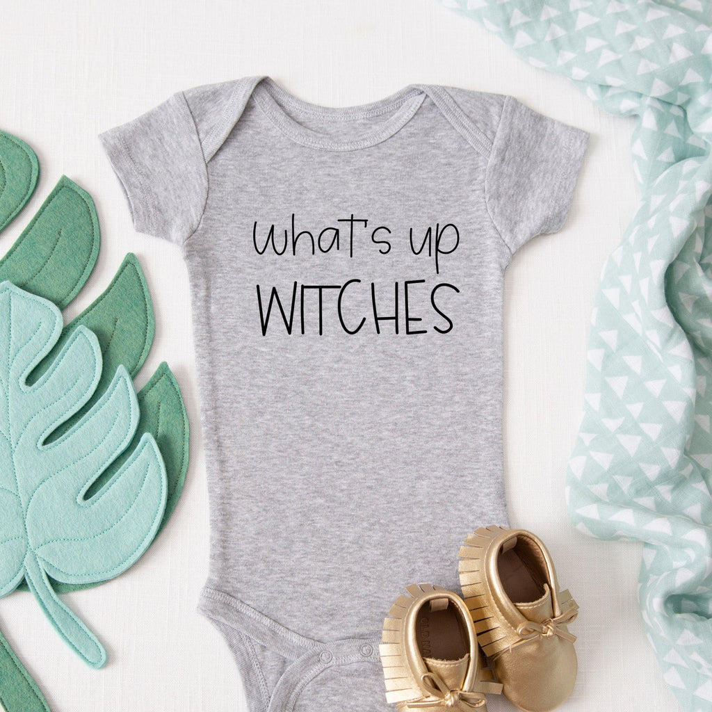What's Up Witches baby bodysuit lifestyle photo - gray bodysuit laid flat on a leaf-print background