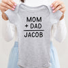Mom + Dad = Baby Name personalized baby bodysuit lifestyle photo - gray bodysuit being held by an adult