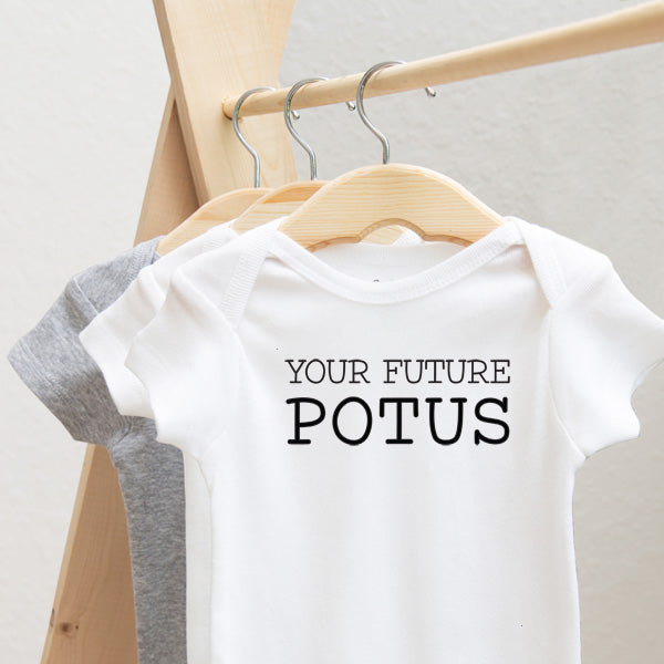Your Future POTUS baby bodysuit lifestyle photo - white bodysuit hanging on a wooden hanger, close-up