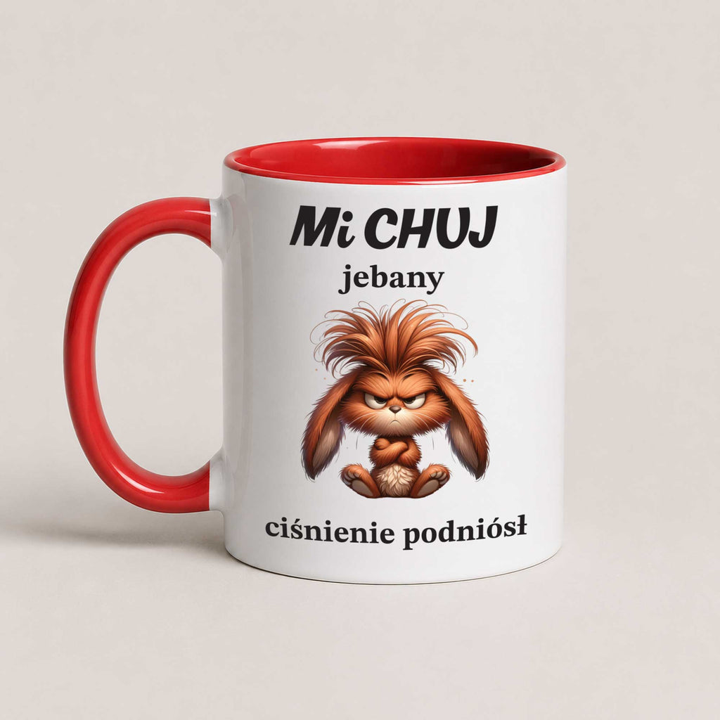 A white ceramic mug with a red handle and red interior, featuring a cartoon brown fluffy creature and Polish text on the front, photographed on a light beige background.