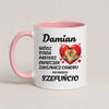 A white ceramic coffee mug with a pink handle and interior, featuring Polish text and a cartoon chameleon inside a red heart on a light beige background.