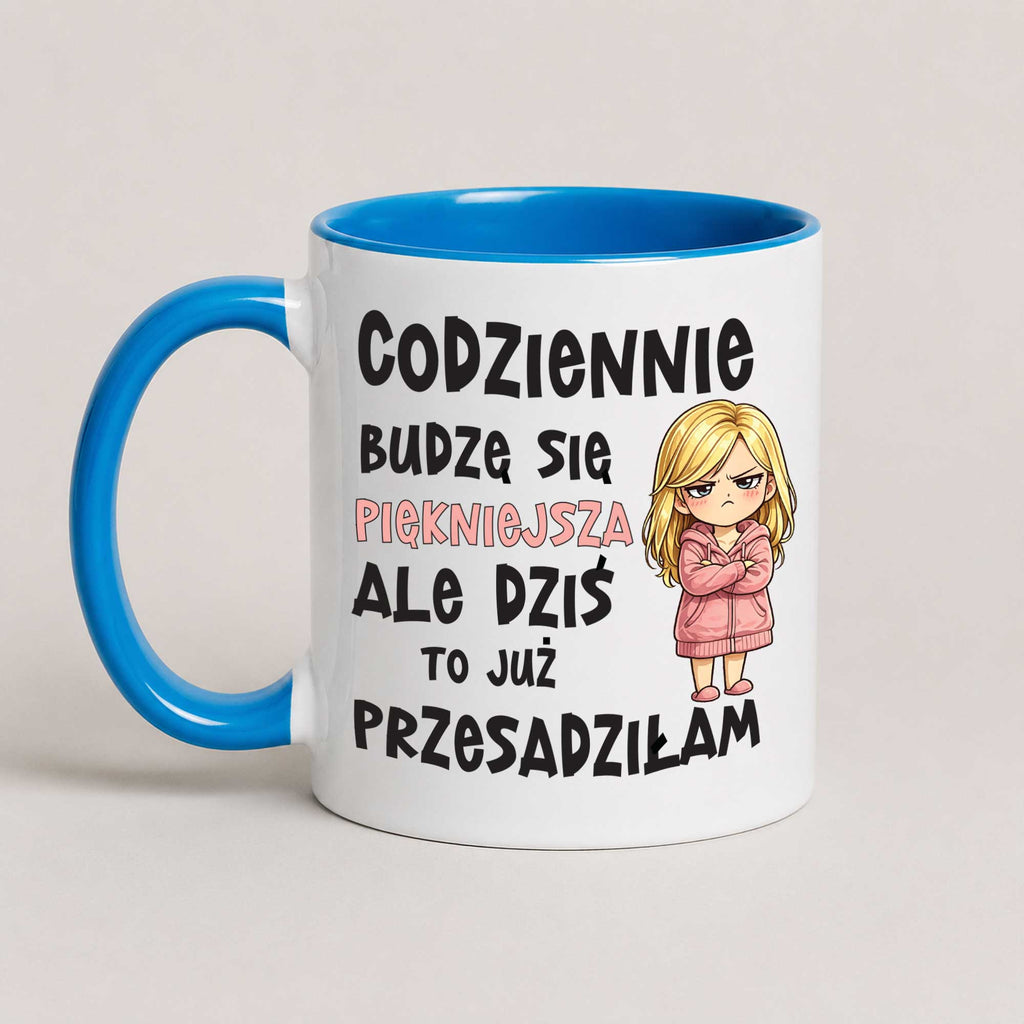 A white ceramic mug with a bright blue handle and interior, featuring Polish text and a cartoon illustration of a blonde girl in a pink robe.