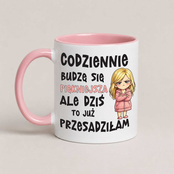 A white ceramic mug with a pink handle and interior, featuring Polish text and a cartoon illustration of a blonde woman in a pink coat.