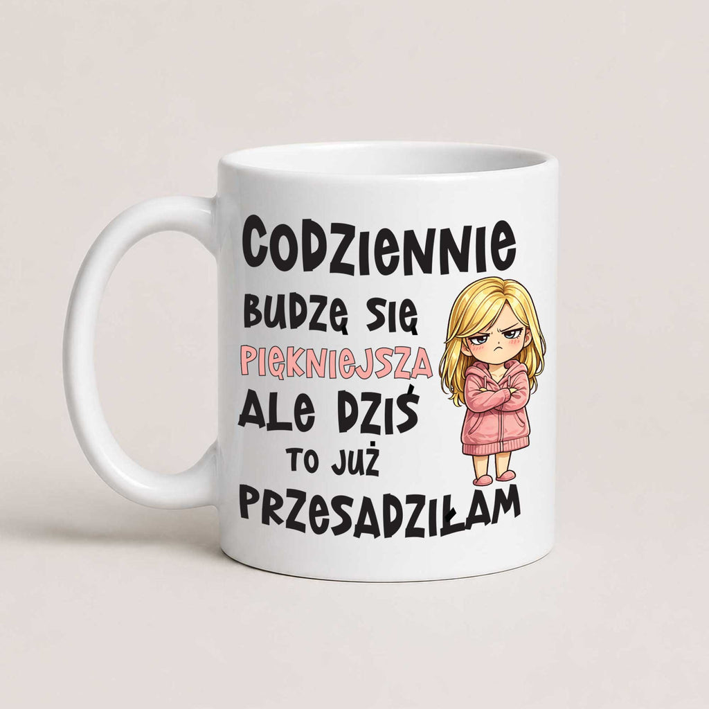 A white ceramic coffee mug with Polish text and a cartoon illustration of a blonde woman in a pink robe, shown on a light beige background.