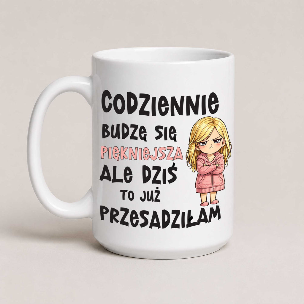 A white ceramic mug with a humorous Polish quote printed in black and pink text, featuring a cartoon illustration of a blonde woman in a pink coat. The mug is photographed against a neutral, light beige background.