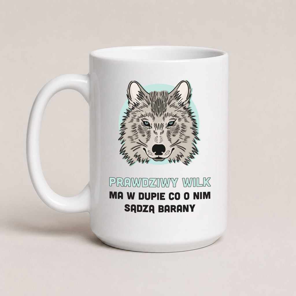 A white ceramic mug with a printed graphic of a wolf's face on a light blue circular background, above Polish text reading 'PRAWDZIWY WILK MA W DUPIE CO O NIM SĄDZA BARANY'. The mug is photographed against a plain, warm off-white background.